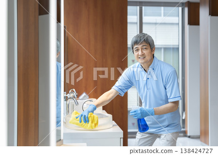 A senior male cleaning staff member smiles and looks directly at the camera. A senior male cleaning staff member smiles and looks directly at the camera. 138424727