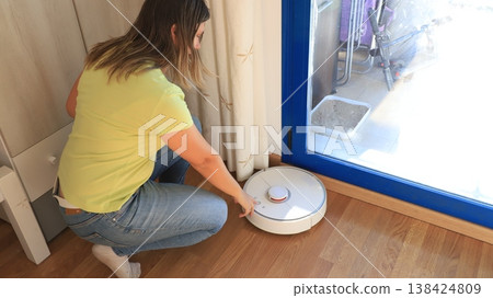 A person is using a robotic vacuum cleaner close to a glass door A person is using a robotic vacuum cleaner close to a glass door 138424809