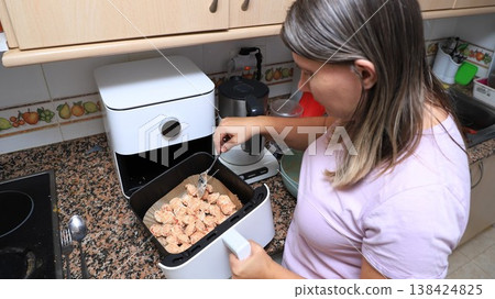 Woman cooking dumplings in an air fryer in a modern kitchen Woman cooking dumplings in an air fryer in a modern kitchen 138424825