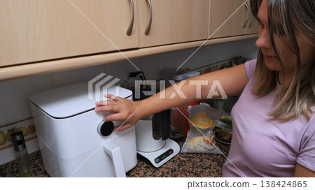 Woman operates a modern air fryer in a contemporary kitchen w 138424865
