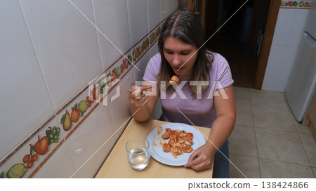 Woman enjoying a meal of dumplimgs while seated at a wooden table in a kitchen Woman enjoying a meal of dumplimgs while seated at a wooden table in a kitchen 138424866
