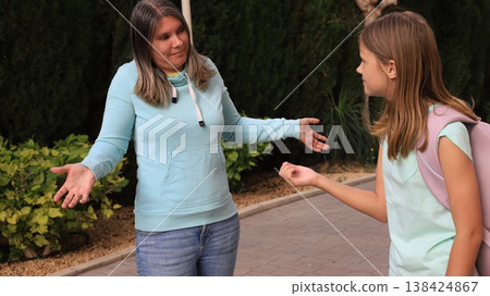 Woman in a light blue hoodie and jeans converses with a girl wearing a light green shirt and backpack Woman in a light blue hoodie and jeans converses with a girl wearing a light green shirt and backpack 138424867