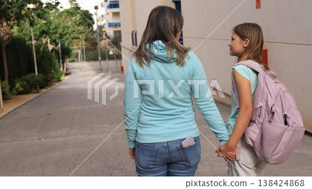Mother accompanying daughter to school, holding hands and smiling outdoors 138424868