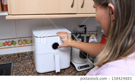 Woman adjusts settings on a modern air fryer in a kitchen with a countertop  138424883