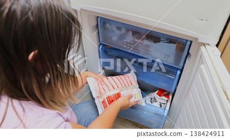 Child with long hair placing food package into freezer compartment of a refrigerator 138424911