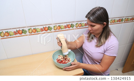 Woman adds mayonnaise to a bowl of dumplings on a wooden table in a kitchen Woman adds mayonnaise to a bowl of dumplings on a wooden table in a kitchen 138424915