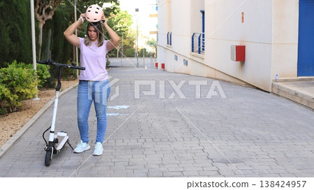 Young woman wearing a helmet prepares to ride an electric scooter on a paved pathway Young woman wearing a helmet prepares to ride an electric scooter on a paved pathway 138424957