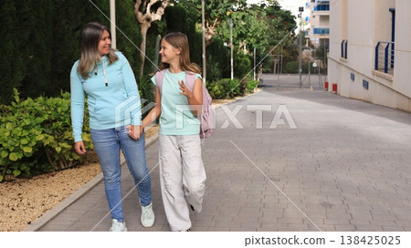 Happy mother and daughter walking together to school, smiling and talking Happy mother and daughter walking together to school, smiling and talking 138425025