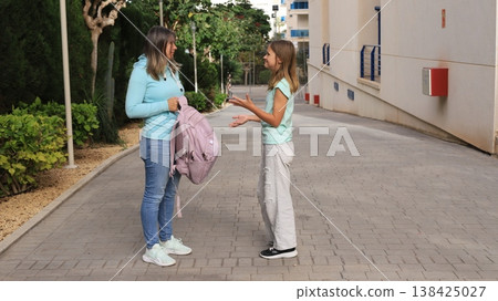 Mother and dougher stand on a paved pathway, one holding a pink backpack while the other gestures 138425027