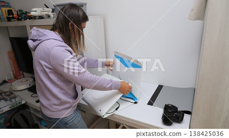 Woman sets up a device on a desk in a home office space while organizing equipment Woman sets up a device on a desk in a home office space while organizing equipment 138425036