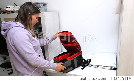 A woman diligently organizes her camera bag at home, getting ready for an exciting outing or event  138425119