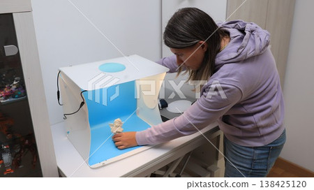 Woman sets up a small studio for taking pictures of objects with a backdrop in a bright indoor space Woman sets up a small studio for taking pictures of objects with a backdrop in a bright indoor space 138425120