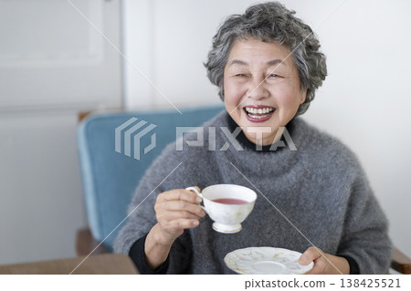 一位微笑的老婦人手捧茶杯。 一位微笑的老婦人手捧茶杯。 138425521