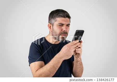 Man Squinting at Smartphone Screen with Vision Difficulty on White Background Man Squinting at Smartphone Screen with Vision Difficulty on White Background 138426177