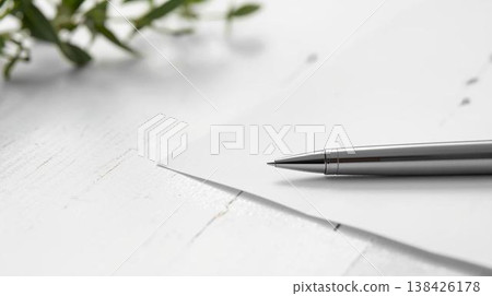 一張白紙和一支銀色原子筆放在白色桌子上，特寫鏡頭，描繪了正在書寫的場景。 138426178