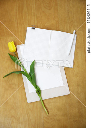 An overhead photograph of a yellow tulip placed on a notebook and paper. 138426343