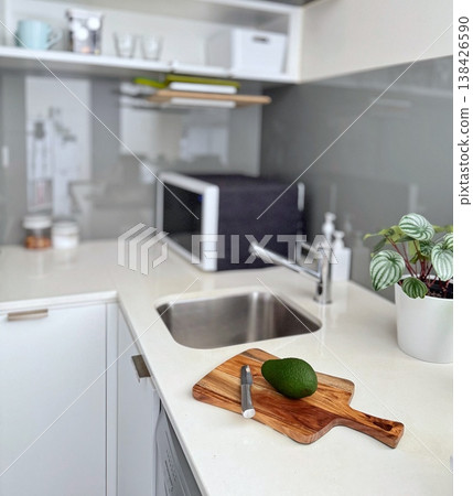 乾淨的白色廚房檯面上放著一塊木質砧板、一個酪梨和一把刀。 138426590