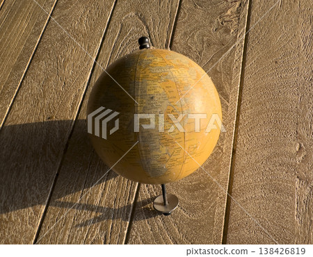 Vintage-style globe standing on a textured wooden surface in warm natural light. Visible map details Vintage-style globe standing on a textured wooden surface in warm natural light. Visible map details 138426819