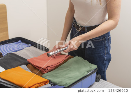 Toothbrush holder and hygiene item go into open suitcase on bed. Cropped female hand places personal 138426920