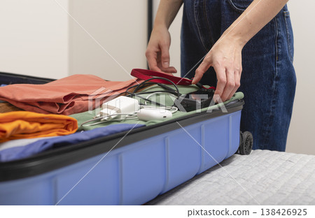 Travel camera and electronic gear lie beside an open suitcase during indoor packing. Cropped female 138426925