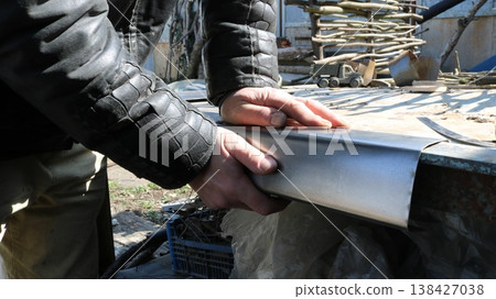 Strong male hands bending a small sheet of metal on an outdoor workbench, manual ironworking in a workshop, bending a piece of metal along the edge of a worktop, the strength of human hands Strong male hands bending a small sheet of metal on an outdoor workbench, manual ironworking in a workshop, bending a piece of metal along the edge of a worktop, the strength of human hands 138427038