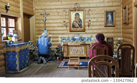 Elderly worshippers pray inside a small wooden chapel, kneeling and seated before an altar. Elderly worshippers pray inside a small wooden chapel, kneeling and seated before an altar. 138427062