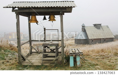 Rustic wooden bell tower with hanging brass bells stands on a frosty hillside. Rustic wooden bell tower with hanging brass bells stands on a frosty hillside. 138427063