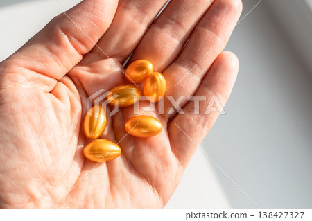 Hand holding shiny golden softgel capsules, representing supplements, vitamins, and medication for health, beauty, and wellness. Healthy lifestyle, self-care 138427327