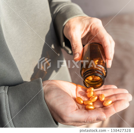 Person pouring orange health capsules from a brown bottle into an open palm, taking daily vitamins for wellness. Healthy lifestyle, self-care 138427328