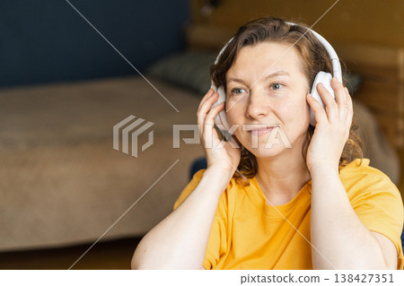 Young woman wearing headphones enjoying audio content at home. Focus on leisure, entertainment, and personal time. Woman listening to music feeling relaxed indoors Young woman wearing headphones enjoying audio content at home. Focus on leisure, entertainment, and personal time. Woman listening to music feeling relaxed indoors 138427351