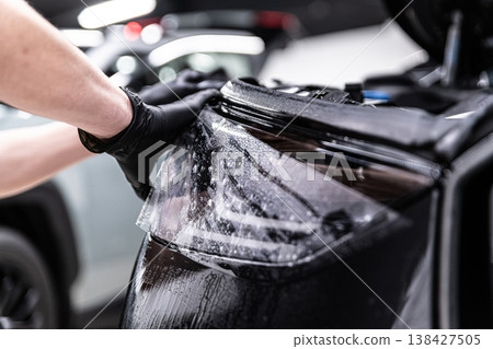 Applying PPF film on car headlights in professional detailing studio 138427505