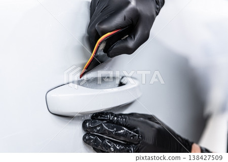 Applying PPF film on car door handle area protection against scratches in detailing studio close-up Applying PPF film on car door handle area protection against scratches in detailing studio close-up 138427509
