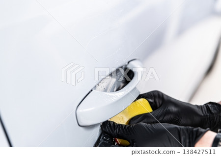 Applying PPF film on car door handle area protection against scratches in detailing studio close-up 138427511