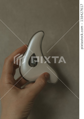 Young woman holding electric guasha face massager over grey stone background, modern microcurrent beauty tool for skin lifting and lymphatic drainage, minimalist self care routine, aesthetic tech. Young woman holding electric guasha face massager over grey stone background, modern microcurrent beauty tool for skin lifting and lymphatic drainage, minimalist self care routine, aesthetic tech. 138427617
