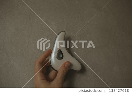 Young woman holding electric guasha face massager over grey stone background, modern microcurrent beauty tool for skin lifting and lymphatic drainage, minimalist self care routine, aesthetic tech. Young woman holding electric guasha face massager over grey stone background, modern microcurrent beauty tool for skin lifting and lymphatic drainage, minimalist self care routine, aesthetic tech. 138427618