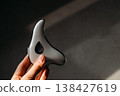 Hand holding modern microcurrent facial massager in warm sunlight with deep shadows, aesthetic beauty tech, minimalist skin care routine at home, sculptural guasha device, moody wellness concept. 138427619