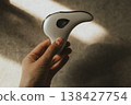 Hand holding modern microcurrent facial massager in warm sunlight with deep shadows, aesthetic beauty tech, minimalist skin care routine at home, sculptural guasha device, moody wellness concept. 138427754