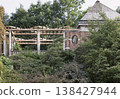 An elegant wooden pergola supported by stone columns stands nestled among lush, overgrown greenery, adjacent to a classic brick garden structure with a prominent shingled roof at The Hill Garden and 138427944