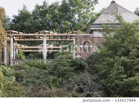 An elegant wooden pergola supported by stone columns stands nestled among lush, overgrown greenery, adjacent to a classic brick garden structure with a prominent shingled roof at The Hill Garden and An elegant wooden pergola supported by stone columns stands nestled among lush, overgrown greenery, adjacent to a classic brick garden structure with a prominent shingled roof at The Hill Garden and 138427944