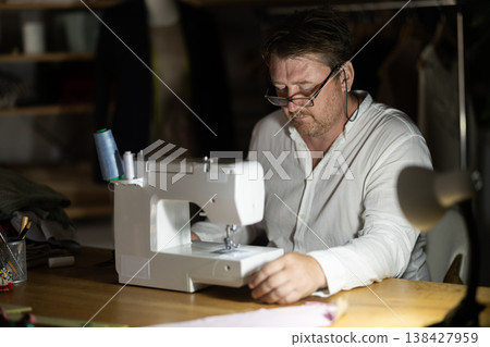Man seamstress operating by sewing machine, manufactures clothing Man seamstress operating by sewing machine, manufactures clothing 138427959