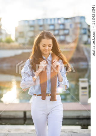 Elegant young woman in old money style walking by riverside near Prague pier during golden hour. Quiet luxury aesthetic and confident European lifestyle concept. Elegant young woman in old money style walking by riverside near Prague pier during golden hour. Quiet luxury aesthetic and confident European lifestyle concept. 138428045