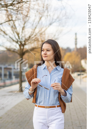 Elegant young woman in old money style holding sunglasses while standing on pier near Prague in early spring. Quiet luxury aesthetic and refined European elegance concept. Elegant young woman in old money style holding sunglasses while standing on pier near Prague in early spring. Quiet luxury aesthetic and refined European elegance concept. 138428047
