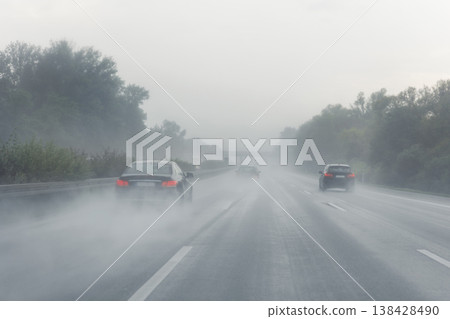 Back tail view of many cars driving fast on wet highway road after rain in Europe. Automobile accident vehicle rush hour collapse. Transportation vacation seasonal stuck. Low visibility bad weather 138428490