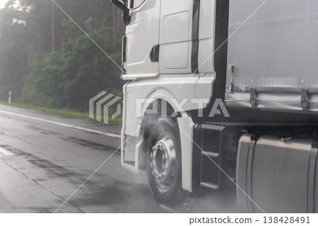 Close-up semi-trailer truck wheel driving fast Splashing Water on Highway, Risk of Aquaplaning on Wet Road. Detail view of hydroplane danger on rainy asphalt surface. Bad dangerous weather conditions 138428491