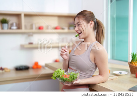 Young woman enjoying a healthy salad in a modern kitchen Young woman enjoying a healthy salad in a modern kitchen 138428535