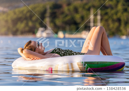 Woman wear green swimsuit relax inflatable ring calm sea near yachts forested coast sunset warm summer sunlight. Female person peaceful moment leisure freedom vacation lifestyle serene getaway mood Woman wear green swimsuit relax inflatable ring calm sea near yachts forested coast sunset warm summer sunlight. Female person peaceful moment leisure freedom vacation lifestyle serene getaway mood 138428536
