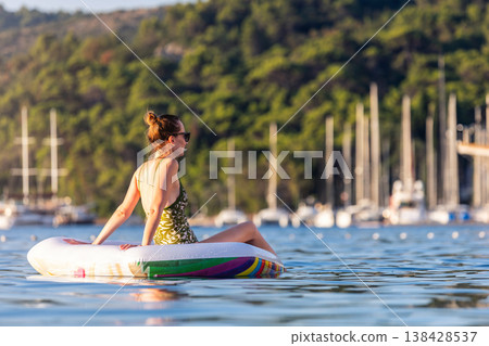 Woman wear green swimsuit relax inflatable ring calm sea near yachts forested coast sunset warm summer sunlight. Female person peaceful moment leisure freedom vacation lifestyle serene getaway mood Woman wear green swimsuit relax inflatable ring calm sea near yachts forested coast sunset warm summer sunlight. Female person peaceful moment leisure freedom vacation lifestyle serene getaway mood 138428537