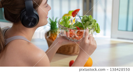 Woman enjoying a fresh salad while wearing headphones 138428550