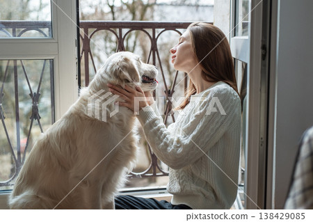 Woman petting golden retriever dog by balcony window Woman petting golden retriever dog by balcony window 138429085