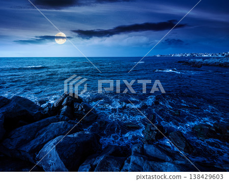 sea coast with stones and boulders at night. view of beach with rock in seaweed. full moon over dynamic cloudscape on the sky above horizon. mysterious summer vacations background concept sea coast with stones and boulders at night. view of beach with rock in seaweed. full moon over dynamic cloudscape on the sky above horizon. mysterious summer vacations background concept 138429603